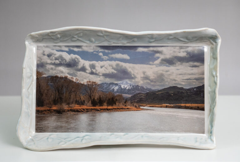 Rectangular tray with color image of scene showing a river with mountains in the distance.